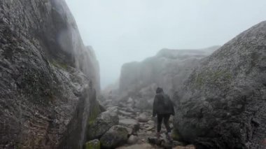 Büyük kayalarla çevrili, sisli kayalık bir kanyonda yürüyüş yapan bir insan..