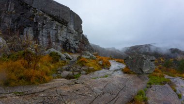 Kayalık arazisi ve sonbahar yapraklarıyla sisli bir dağ manzarası. Sahnede, sis ve bulutlarla çevrili engebeli çevreye uzanan büyük bir kaya oluşumu ve yol yer alıyor..