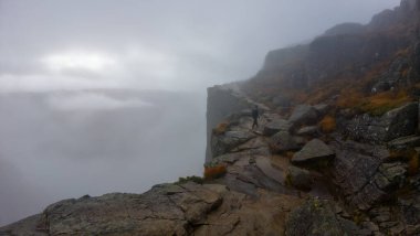 Sis içinde gizlenmiş kayalık bir uçurum kenarında yürüyen bir insan gizemli ve maceracı bir atmosfer yaratır..