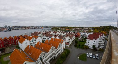 Kırmızı çatılı evleri ve bulutlu gökyüzünün altında bir nehri olan kıyı kasabasının havadan görüntüsü..