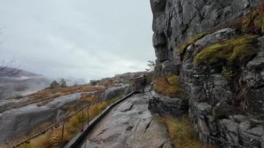 Üzerinde bulutlu bir gökyüzü olan kayalık bir uçurum boyunca dar ahşap bir köprü..