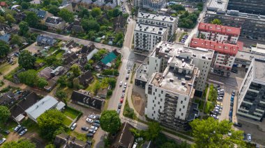 Modern apartman kompleksleri ve eski evler de dahil olmak üzere sokakları ve park halindeki arabaları görülebilen şehir manzarası.