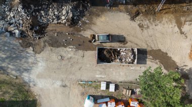 Çöp konteynırına enkaz yükleyen bir kamyonun bulunduğu inşaat alanının havadan görüntüsü..