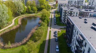 Küçük bir gölet ve yeşil park alanının yanındaki modern konut binalarının hava manzarası..