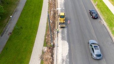 Yol üzerinde çalışan sarı kazıcılı bir inşaat alanının havadan görüntüsü. Bir işçi kaldırım inşa ediyor..