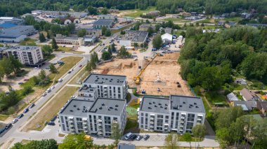 Modern apartman binaları ve çevreleyen yeşilliklerin bulunduğu bir yerleşim alanındaki inşaat alanının havadan görüntüsü..