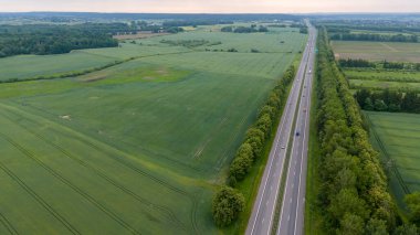 Uçsuz bucaksız yeşil tarlalar ve ormanlardan geçen düz bir otoyolun havadan görünüşü..