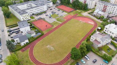 Koşu pisti olan bir okul spor kompleksinin havadan görünüşü, binalar ve ağaçlarla çevrili futbol sahası..