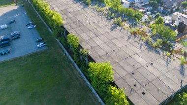 Terk edilmiş bir binanın çatısı ekili, otopark ve yerleşim yerleriyle çevrili..