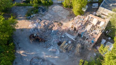 İnşaat alanının havadan görüntüsü kısmen yıkılmış bir bina enkaz ve inşaat malzemeleriyle çevrili. Ağır makineler görünür durumda ve ağaçlar bölgeyi çevrelemiş durumda..