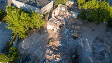 Ağaçlar ve enkazlarla çevrili yıkılmış bir binanın havadan görüntüsü..