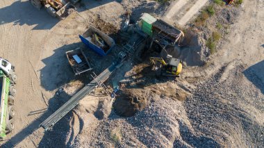 Ağır makineler, çakıl ve kum yığınları olan bir taş ocağının hava görüntüsü..