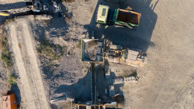 Ağır makineler, çakıl ve kum yığınları olan bir taş ocağının hava görüntüsü..