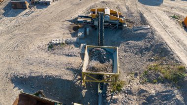 Taşıma bantları ve çakıl yığınları olan çakıl işleme fabrikasının hava görüntüsü.