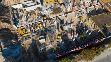 Çeşitli makine ve yapı malzemeleriyle büyük bir inşaat alanının havadan görüntüsü. Site vinçler, iskeleler ve inşaat faaliyetleriyle meşgul..