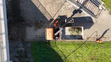 Kaldırımda bir kazıcı çalıştıran inşaat işçilerinin hava görüntüsü. Kazıcı eski bir kaldırımın üzerinde, etrafında çimenler ve kaldırımlar var..