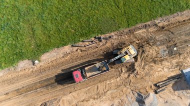 Kırmızı bir çöp kamyonuna kum yükleyen bir buldozerin bulunduğu inşaat alanının havadan görüntüsü..