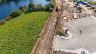 Su birikintisinin yakınındaki bir inşaat alanının havadan görünüşü kısmen inşa edilmiş bir yol, yeşil çimenler ve inşaat ekipmanlarını gösteriyor..