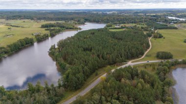 Sarmal yollarla çevrili yemyeşil bir ormanın ve bulutlu bir gökyüzünün altında sakin bir gölün havadan görünüşü..