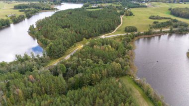 Çevresi iki gölle çevrili yemyeşil bir ormanın havadan görünüşü, kıvrımlı bir yol manzarayı kesiyor. Sahne, yoğun ağaçlar ve sakin suyla doğanın huzurunu yakalıyor..