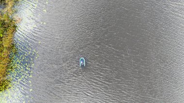 Su zambaklarıyla çevrili bir göldeki küçük bir kayıktaki insanın havadan görüntüsü..