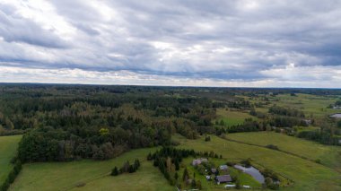 Tarlaları, ormanları ve bulutlu bir gökyüzünün altında küçük bir göleti olan kırsal bir arazinin havadan görünüşü..