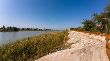 Taştan geçitli, yemyeşil bir nehir manzarası ve açık mavi bir gökyüzü..