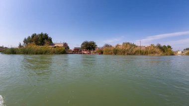 Bereketli yeşil bir nehir manzarası ve berrak mavi bir gökyüzü, nehir kıyısı boyunca küçük bir yerleşim yeri.
