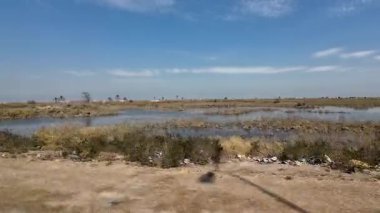 Derme çatma metal bir barınağı ve açık mavi bir gökyüzünün altında çiti olan kırsal bir arazi..