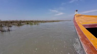 Ahşap bir tekne, berrak mavi bir gökyüzünün altında, sakin bir nehirde yol alır..