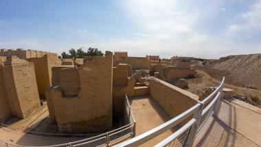 Duvarları tuğlalı, ön planda metal korkulukları olan, berrak mavi gökyüzünün altında antik kalıntıların panoramik görüntüsü..