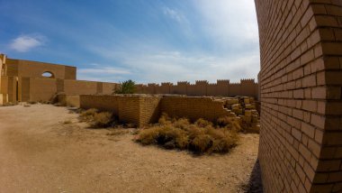 Mavi gökyüzünün altındaki eski tuğla duvarlar ve kalıntılar, çöl ortamında dağınık bitki örtüsü..