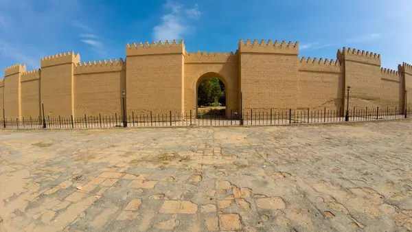 Yenilenmiş eski bir tuğla duvar ve berrak mavi gökyüzüne karşı dizilmiş kemerli bir giriş. Ön planda girişe giden bir kaldırım taşı yolu var..