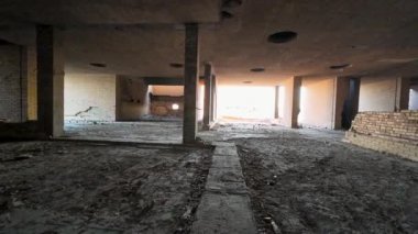 Terk edilmiş bina içi, tuğla duvarlar ve toprak zemin açık bir girişten gelen güneş ışığıyla aydınlatılmış..