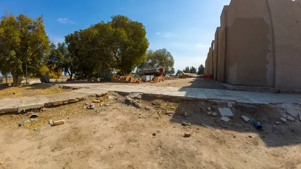 Mavi gökyüzünün altında kısmen inşa edilmiş bir yapı, ağaçlar ve dağınık döküntüler olan bir inşaat alanı..