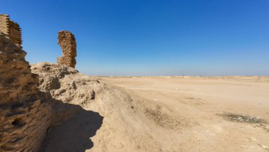 Açık mavi gökyüzünün altındaki çöl arazisindeki antik bir yapının kalıntıları..