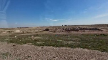 Uçsuz bucaksız, açık bir arazi, kuru, çorak arazi ve açık mavi gökyüzünün altında yeşil çimenler..