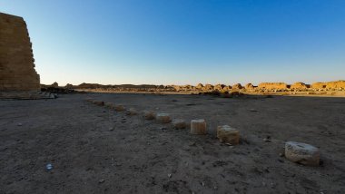 Dağılmış taş sütunları ve berrak mavi gökyüzü ile çöl manzarasında antik kalıntılar..