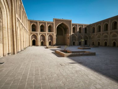 Açık mavi gökyüzünün altında karmaşık tuğla ve kemerlerle dolu tarihi bir avlu..