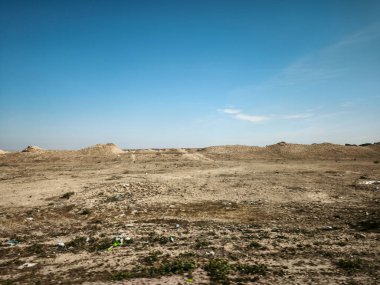 Açık mavi gökyüzünün altında dağınık enkazlarla çorak bir çöl manzarası..