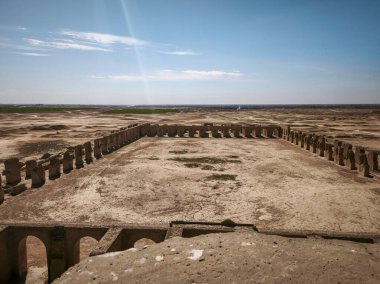 Açık mavi gökyüzünün altında çöl manzarasında sütunları olan dikdörtgen bir yapının antik kalıntıları..