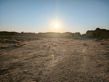 Kıraç bir çöl üzerinde gün batımı kayalık oluşumlar ve seyrek bitki örtüsüyle.