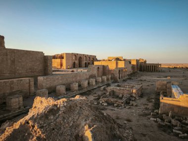 Temiz mavi gökyüzünün altında taş yapılar ve kemerler olan tarihi bir yerin kalıntıları..