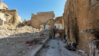 Açık mavi gökyüzü altında yıkılan binalar ve enkazlarla savaştan zarar görmüş bir şehir manzarası..