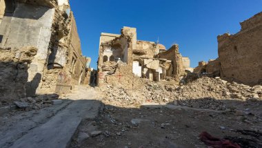 Açık mavi gökyüzü altında yıkılan binalar ve enkazlarla savaştan zarar görmüş bir şehir manzarası..