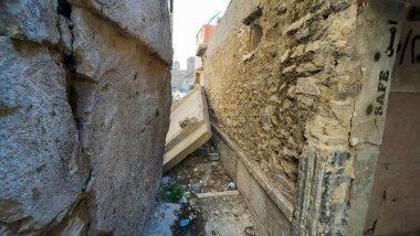 Enkaz ve duvar yazısıyla dolu eski taş binalar arasında dar bir ara sokak..