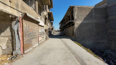 Eski, yıpranmış binalarla dar sokaklar ve uzakta park edilmiş bir araba..