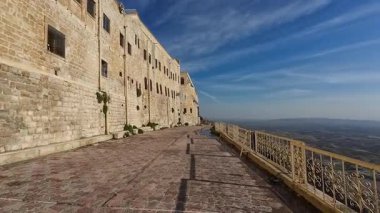 Kemerli camları olan tarihi bir taş bina mavi gökyüzünün altında geniş bir araziye bakıyor..