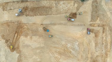 Toprağı hareket ettiren kamyonları ve makineleri olan bir inşaat alanının havadan görüntüsü.