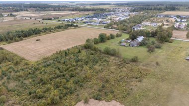 Tarlaların, dağınık ağaçların ve arka planda küçük bir köyün bulunduğu kırsal bir arazinin havadan görünüşü. Ön planda yeşillik ve tarım arazilerinin karışımı görünüyor..
